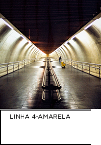 Fotografia. Túnel de metrô iluminado. Abaixo “LINHA 4-AMARELA”.