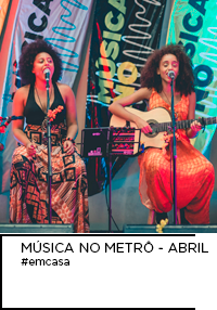 Fotografia. Giselle e Mariana Sancar do duo Amanas se apresentando no palco Música no Metrô, estação Vila Prudente. Abaixo “MÚSICA NO METRÔ - ABRIL #emcasa”