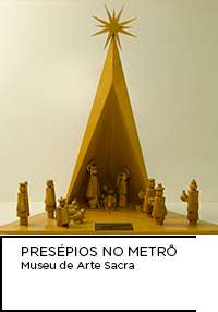 Fotografia de presépio de formato triangular feito em madeira com cores naturais do material. Abaixo: PRESÉPIOS NO METRÔ. Museu de Arte Sacra
